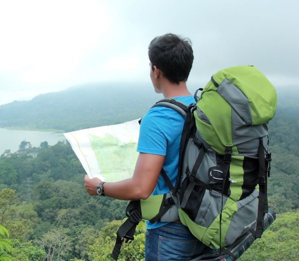 Mand med rejserygsæk læser et kort med en flot udsigt udover bjerge og vand